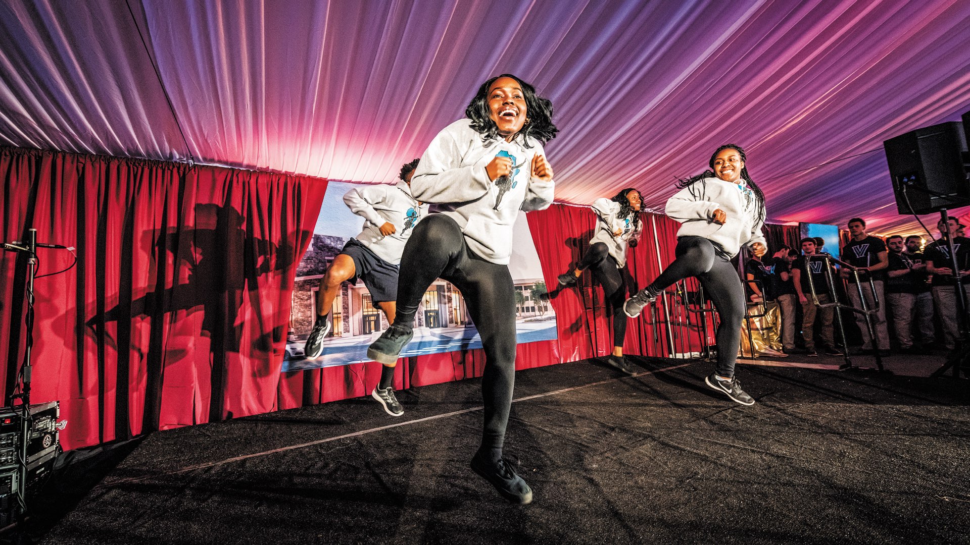 Four members of Villanova’s Wazobia African Dance Company, smiling and in mid dance, with feet a few inches off the ground