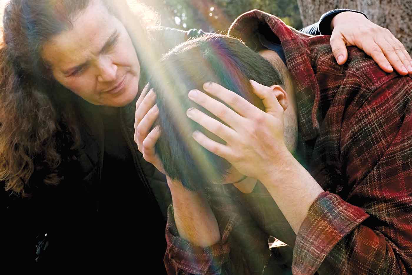 Women putting a comforting arm around a man who's holding his head looking down