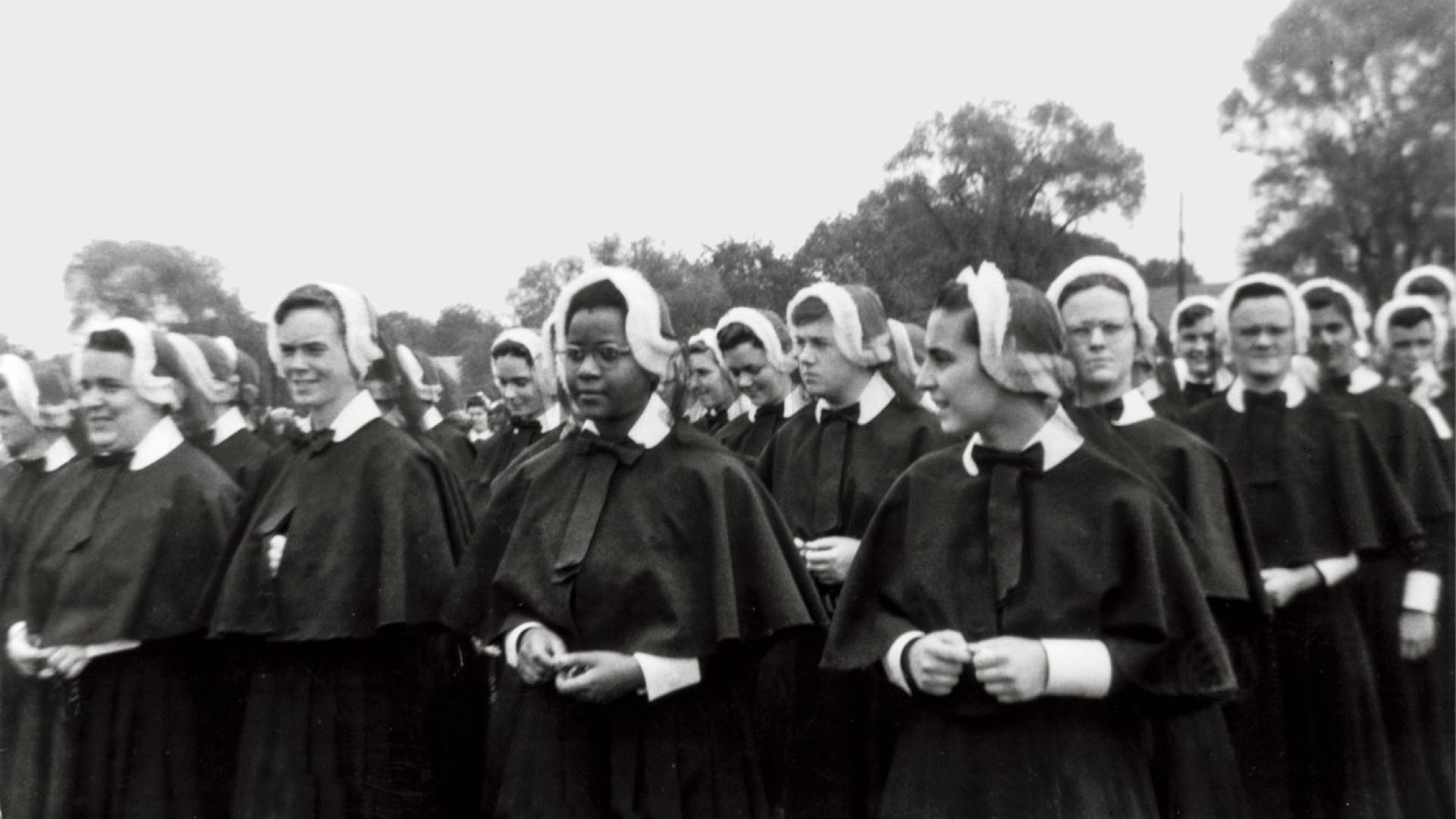A black-and-white photo of a young Sister Cora Billings in habit amid a large crowd of novitiate nuns