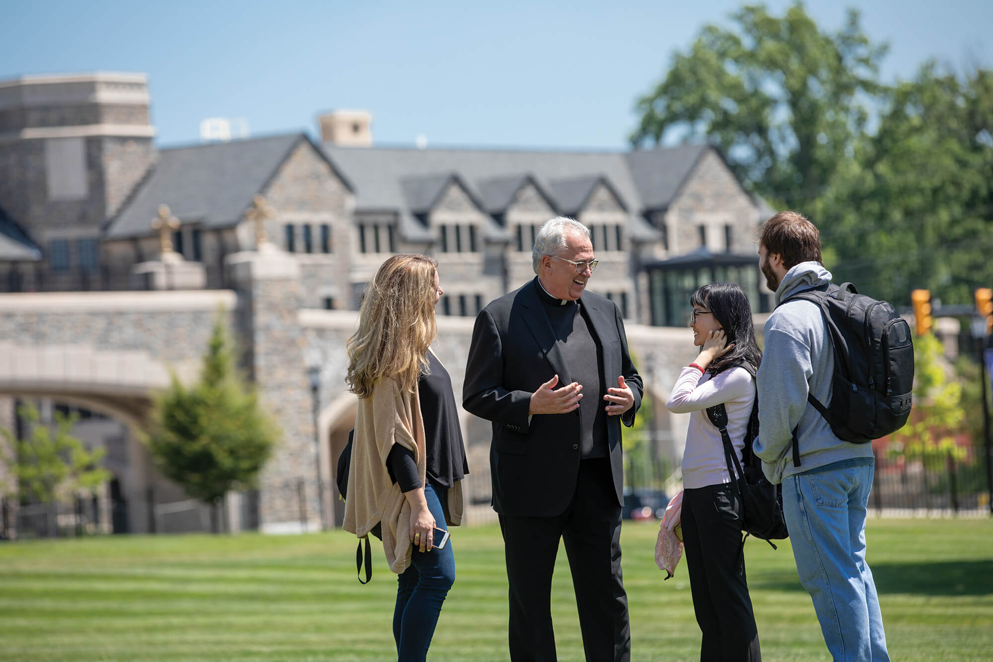 priest smiling and conversing with students outside