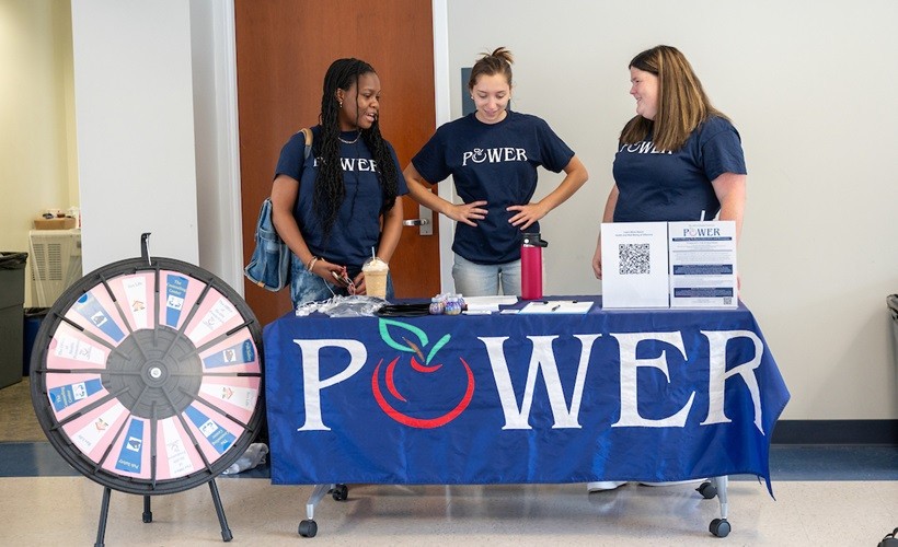 Peers Offering Wellness Education and Resources Three students staff a POWER table at a campus event