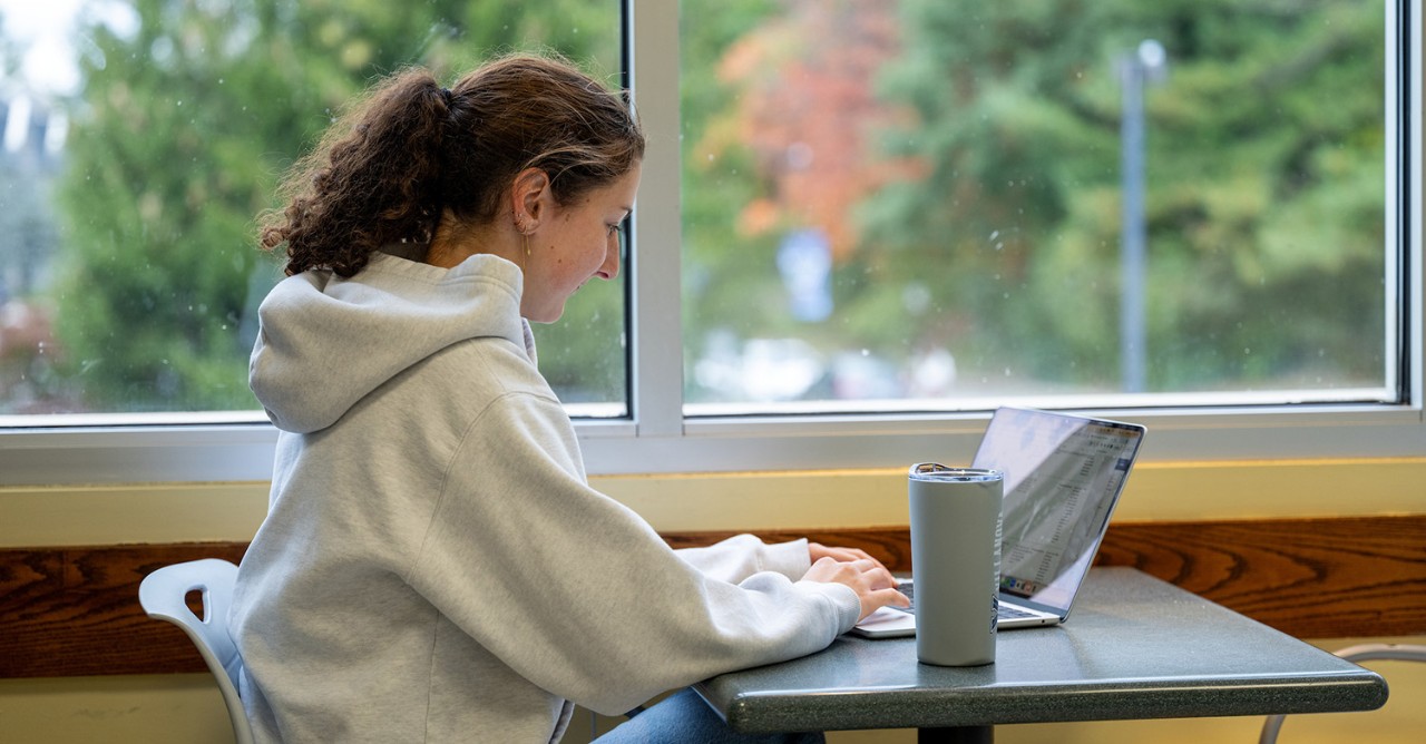 Student working on laptop sitting at a table Student working on laptop sitting at a table