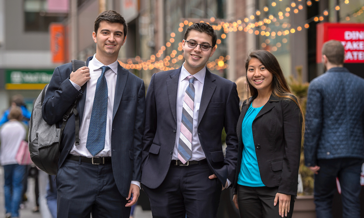 Three young people standing next to each other in business atire with lights behind them