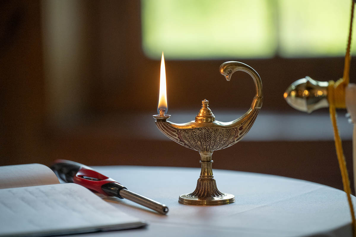 A lit lamp placed on a table with a lighter and prayer sheets