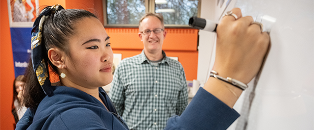 Image of a Villanova student writing on a dry erase board during class