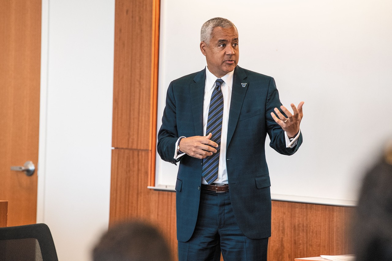 Mark C. Alexander speaking in a classroom dressed in a blue suit and tie 
