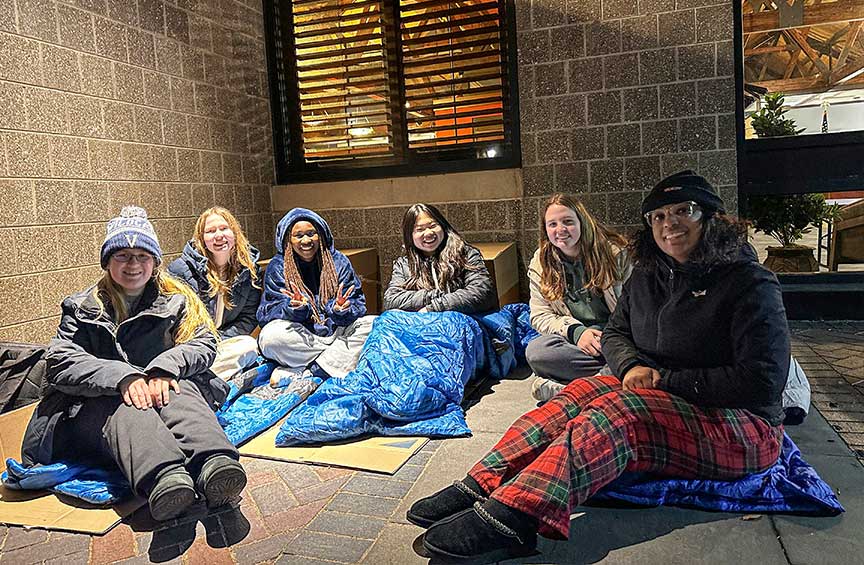 Six students in sleeping bags participate in the Hunger and Homelessness Awareness Week Sleep Out, gathered outside at night.